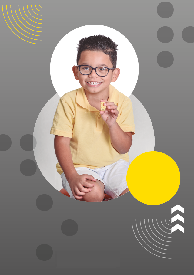 Imagem: Fotografia. Menino de cabelos curtos e castanhos usa óculos com armação preta, camisa polo amarela e bermuda branca, está sentado, sorri e segura com a mão esquerda uma peça de Lego Braille Bricks, um pequeno bloco de montar amarelo, próximo ao peito. O fundo é cinza com círculos em branco e amarelo, pontos em braille, setas brancas e linhas curvadas em branco e amarelo. Fim da imagem.