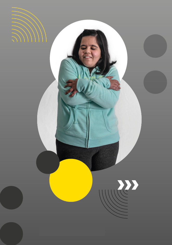Imagem: Fotografia. Menina de cabelos pretos lisos, na altura dos ombros, veste um moletom verde com zíper e capuz e calça preta. Ela está de pé com os braços cruzados sobre o peito e os olhos fechados; sorri. O fundo é cinza com círculos em branco e amarelo, pontos em braille, setas brancas e linhas curvadas em preto e amarelo. Fim da imagem.