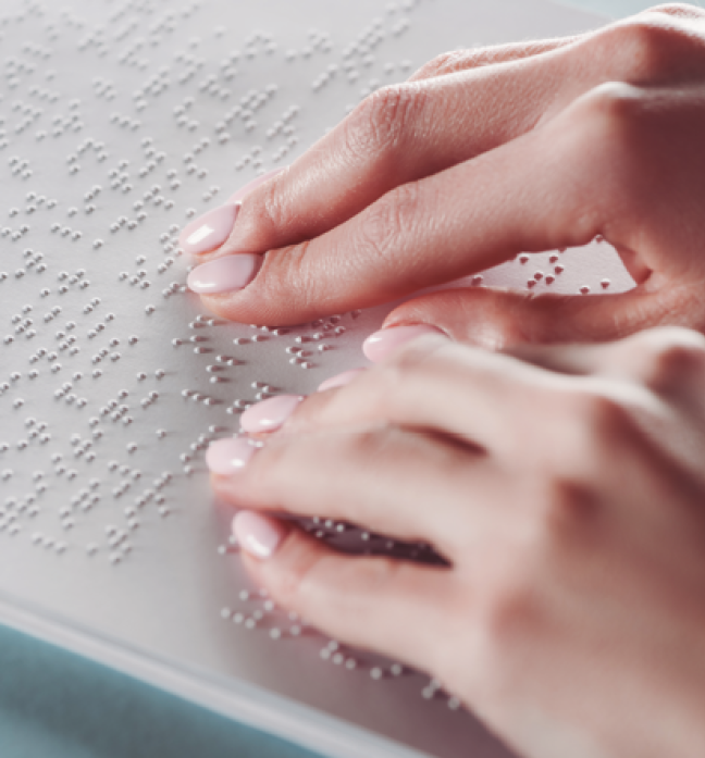 Imagem: Fotografia. Destaque para as mãos de uma pessoa, os dedos tócam uma superfície com relevo em escrita braille. Fim da imagem.