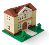 image: Photograph. A two-story building made of building blocks, predominantly beige with brown details on the roof and base. There are white windows on each floor and a brown arched door at the entrance. In front, there is a white path leading to the door, surrounded by green areas made of pieces that imitate grass and small bushes. end of image.