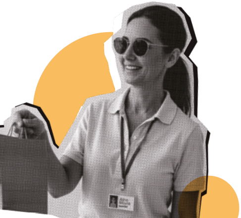 Imagem: Fotomontagem. Fotografia em preto e branco, destaque para o torso de uma mulher com cabelos escuros presos em um rabo de cavalo, usa óculos escuros, camiseta polo clara e crachá no pescoço. Ela segura uma sacola de papelão na mão e sorri. Ao fundo, dois círculos amarelos, um grande e um pequeno. Fim da imagem.