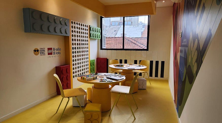 Foto mostra a sala do projeto LEGO Braille Bricks. Ao centro, duas mesas com os kit do LEGO Brille Bricks,