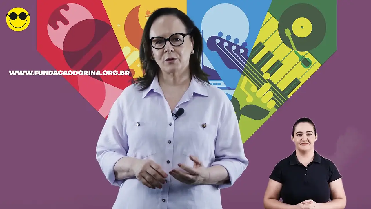 Uma mulher, Ika Fleury, com uma camisa roxa clara está em frente a um fundo colorido e abstrato com ilustrações de instrumentos musicais. O URL de um site está visível à esquerda. No canto, uma mulher de preto usa linguagem de sinais.